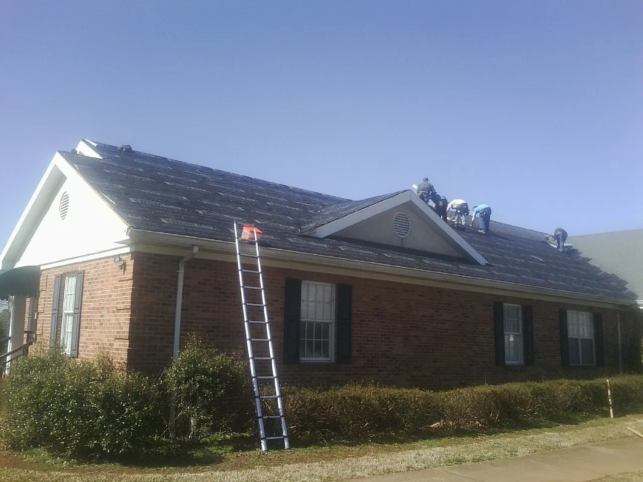 Crew tearing shingles off a brick ranch roof with a ladder set — Emergency Roof Repair work by our crew in Menahga