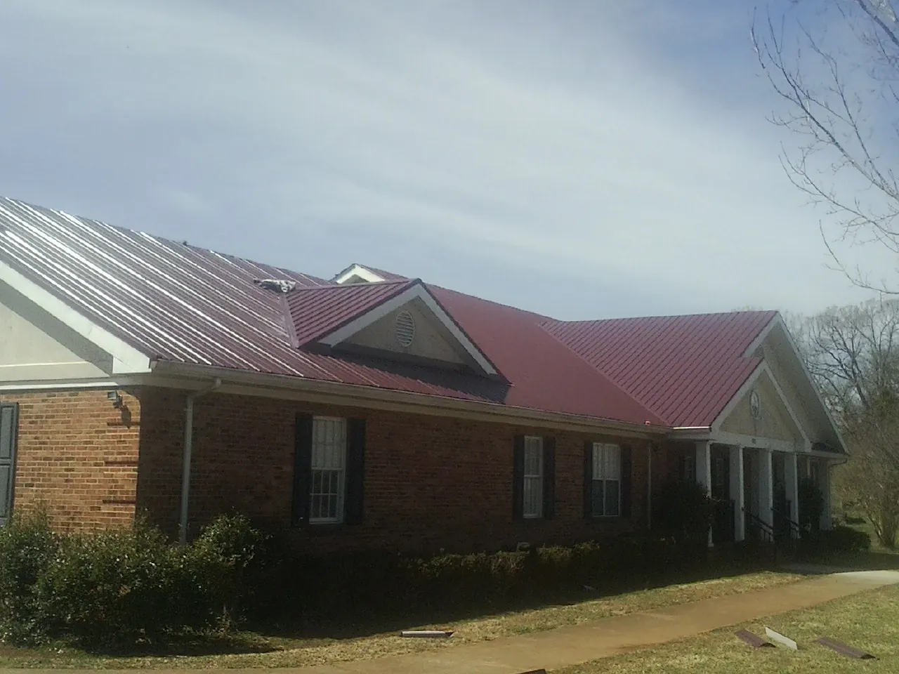 Red metal roof with gabled entries on a long brick building, from a Hail Damage Roof Repair job in Menahga
