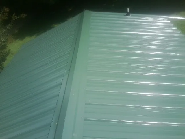 New green metal panels meeting at the ridge of a roof — Flat Roof Repair work by our crew in Menahga
