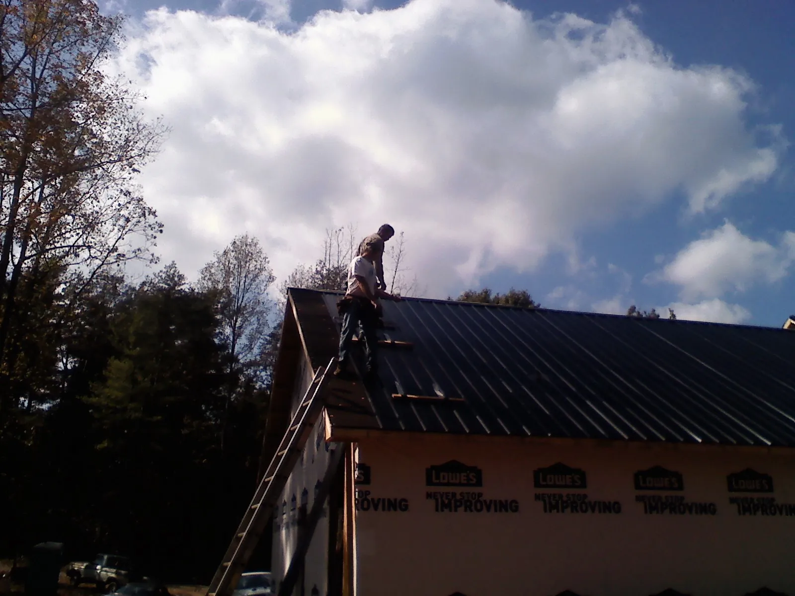Roofer fastening dark metal panels high against a cloudy sky, from a Roof Inspection job in Menahga
