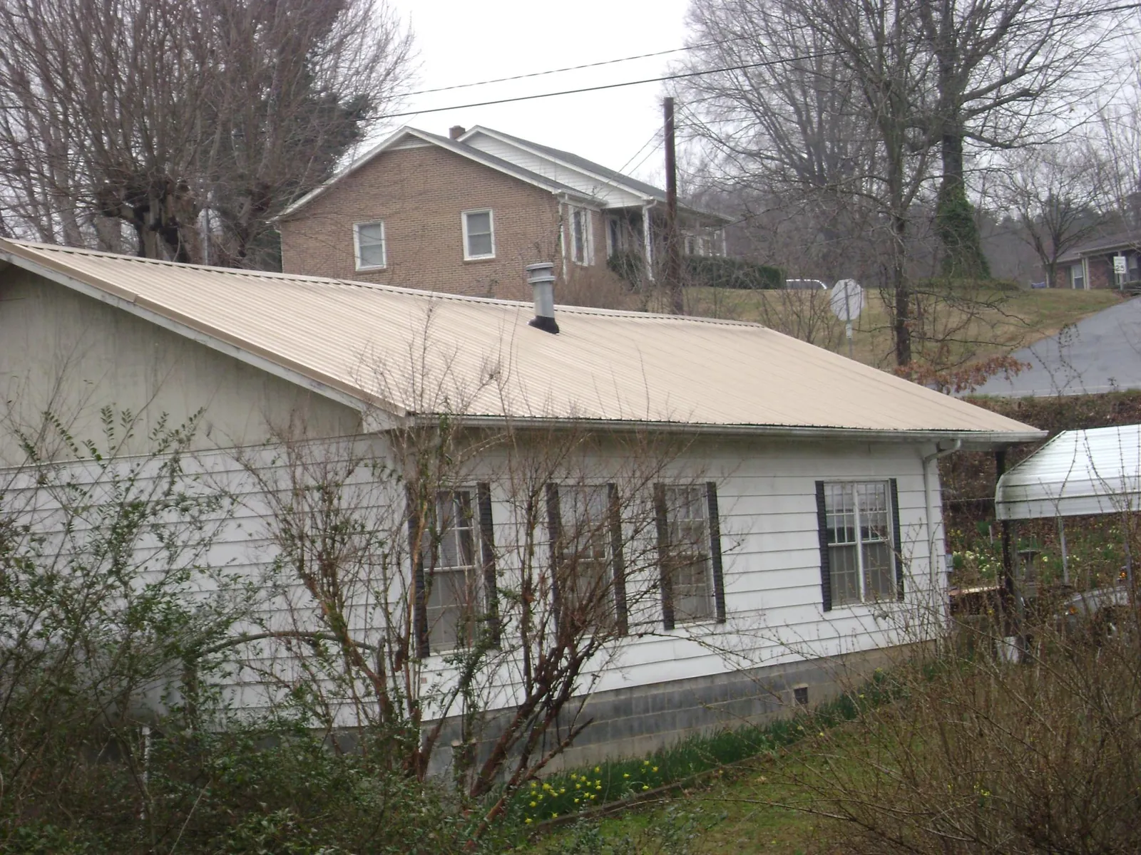 Tan metal roof on a white sided house set into a hillside — Commercial Roofing by Roofing Brothers in Menahga